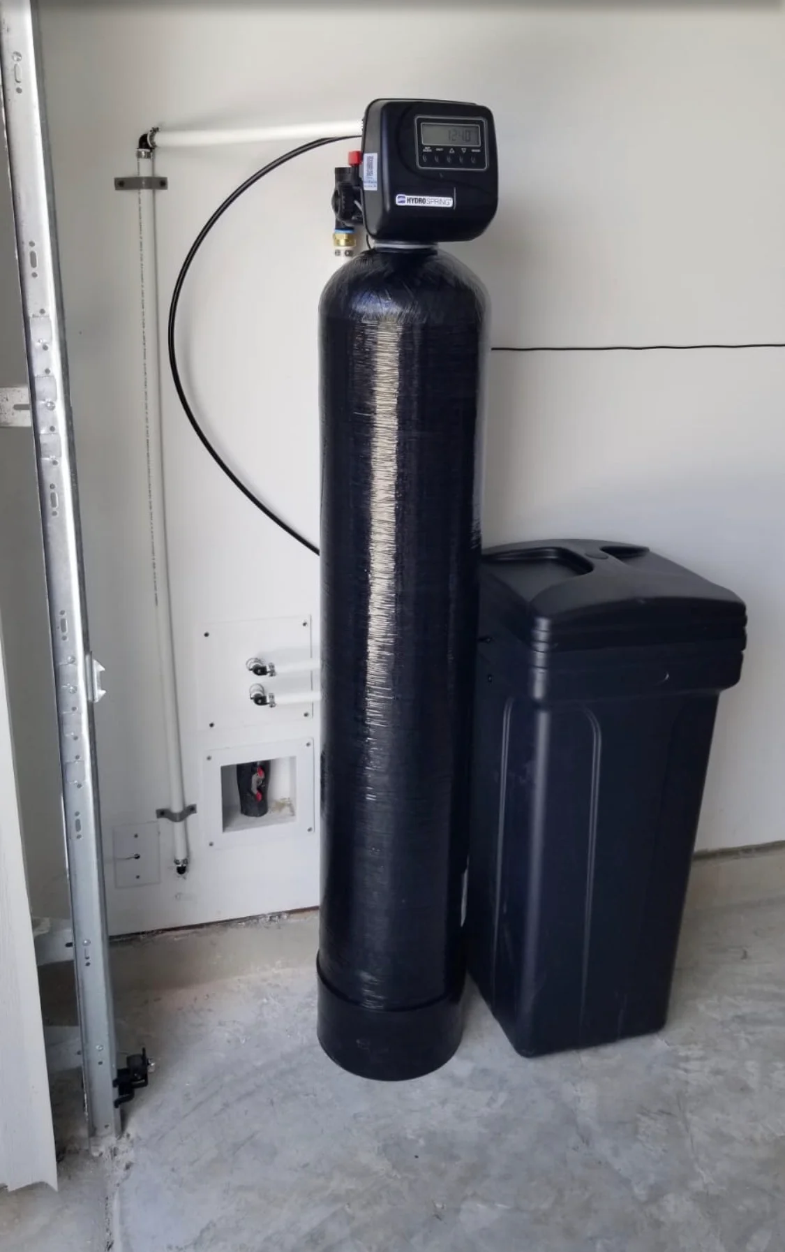Black water softener tank with digital control valve and brine tank installed in utility room